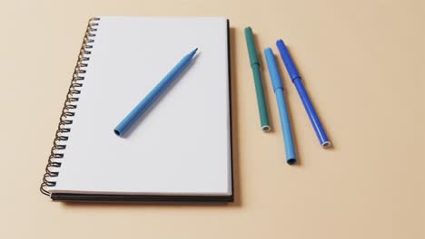 close up of blue markers with notebook on beige background, in slow motion