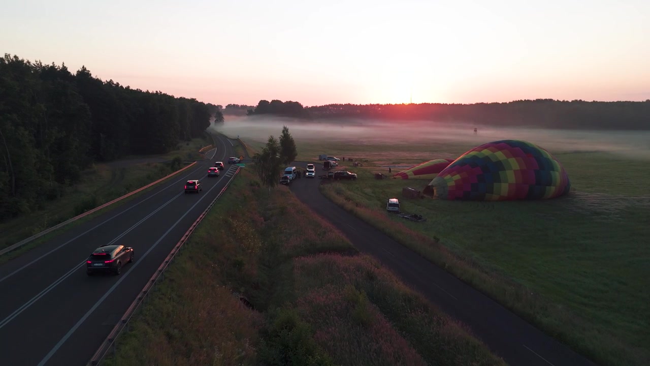 Vista aerea di una mongolfiera che si gonfia in un campo accanto a un'autostrada durante un'alba nebbiosa. Concetto cinematografico di viaggio e avventura.