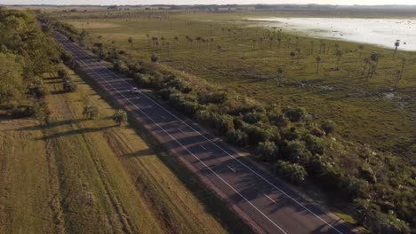 Drone-Pov-De-Coche-Blanco-Aislado-Conduciendo-A-Lo-Largo-De-La-Carretera-Rural-Rectilínea-De-Uruguay-Cerca-De-La-Laguna-Negra