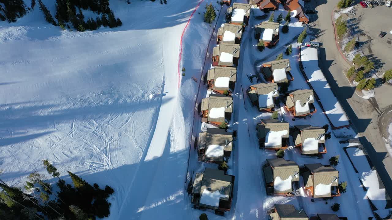 Overhead drone view of snow-covered condos in a mountain forest, with frosty rooftops, powder-lined streets, and pine trees creating the perfect winter vacation setting