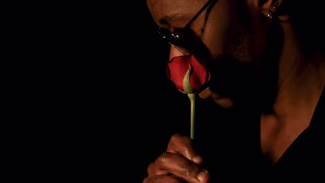 stylish man smelling - rubbing rose against cheeks, profile close up, black background