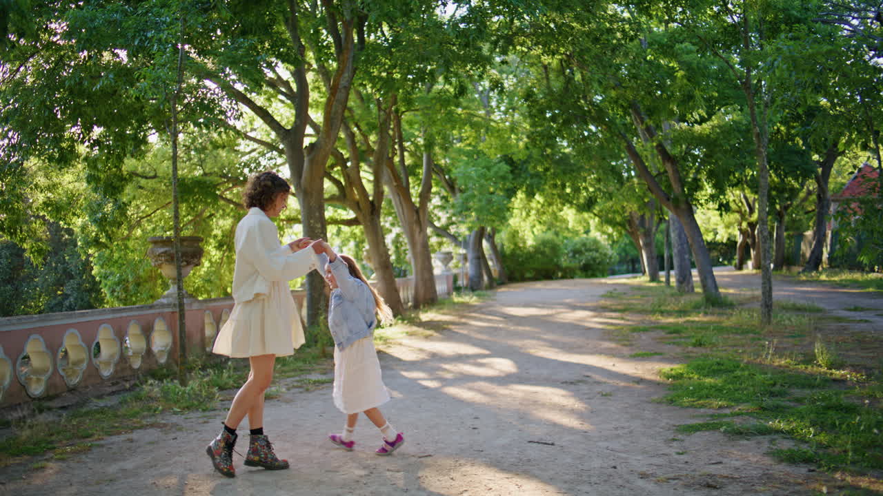 Mother daughter swirling sunny garden at family weekend. Woman spinning girl