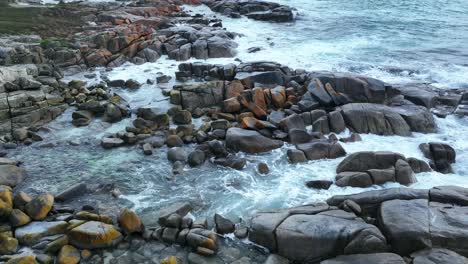 Aerial-shot-above-a-section-of-the-Orange-coloured-boulders-of-the-Bay-of-Fires