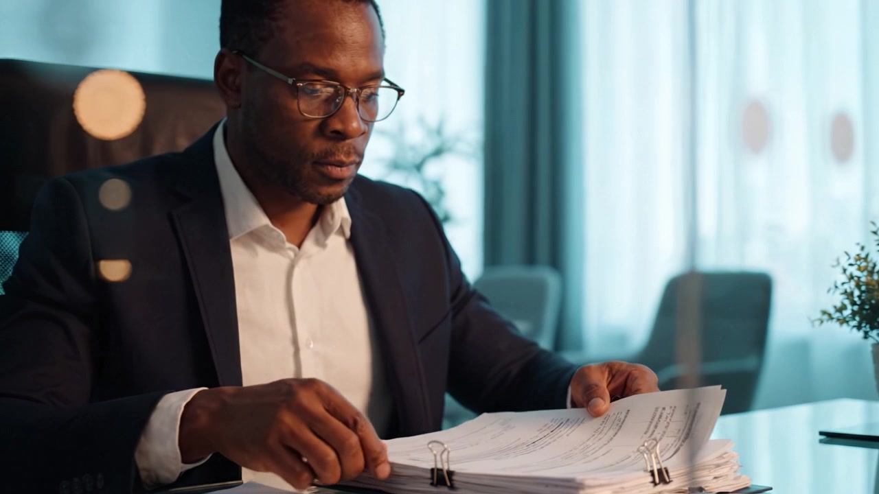 Focused Professional Reviewing Documents in Modern Office Setting, Highlighting Dedication and Attention to Detail While Using Paperwork and Binder Clips