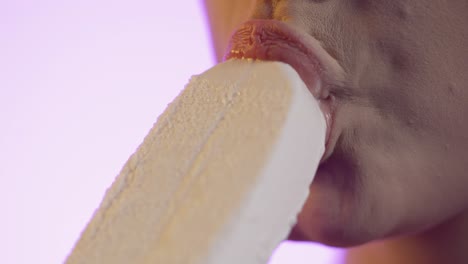 close up of woman's mouth and lips eating white popsicle ice cream with pink background, studio shot