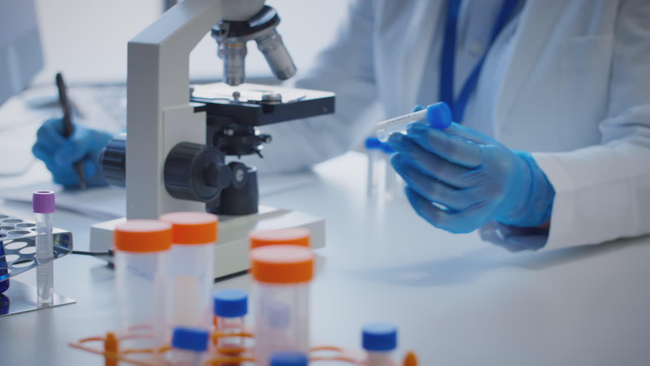 primer plano de un trabajador de laboratorio que lleva a cabo investigaciones utilizando un microscopio con un tubo de ensayo etiquetado lambda