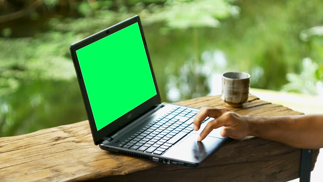 Hand man using laptop with green screen on wooden desk with cup of drink near pond