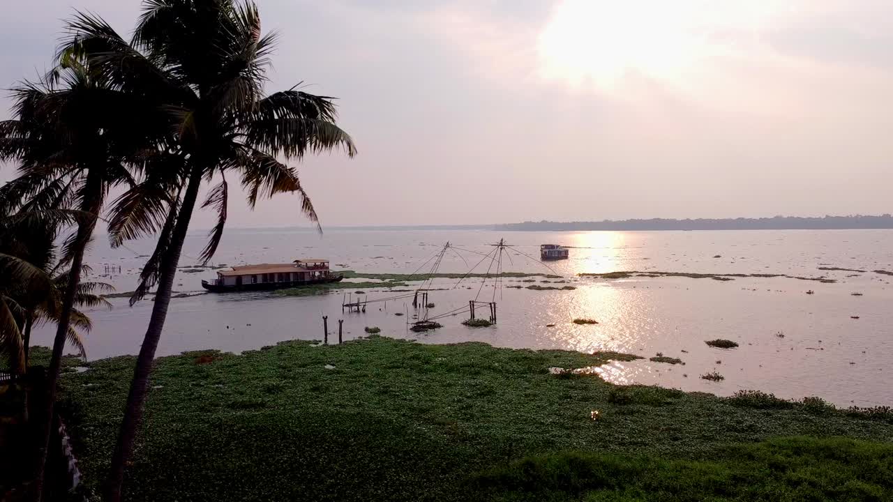 Tropical view of Kerala backwaters at sunrise sunset with palm trees framing a houseboat and Chinese fishing net