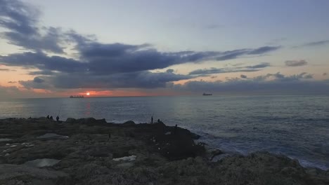aerial flight towards and above fishermen fishing on shore of sea water at sunset