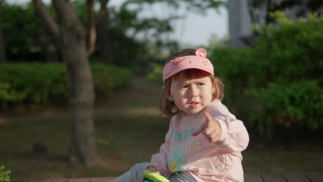 Young-Korean-Ukranian-girl-sitting-on-dock-holding-toys,-pointing