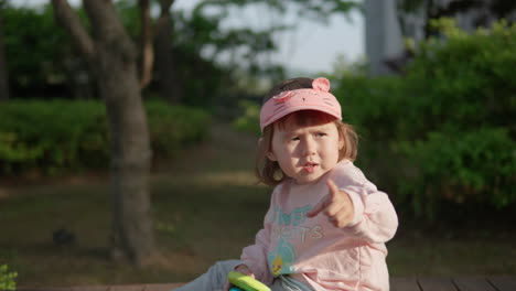 young korean-ukranian girl sitting on dock holding toys, pointing