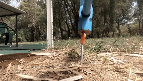 hammering an orange tent peg in the dry ground with a blue hammer