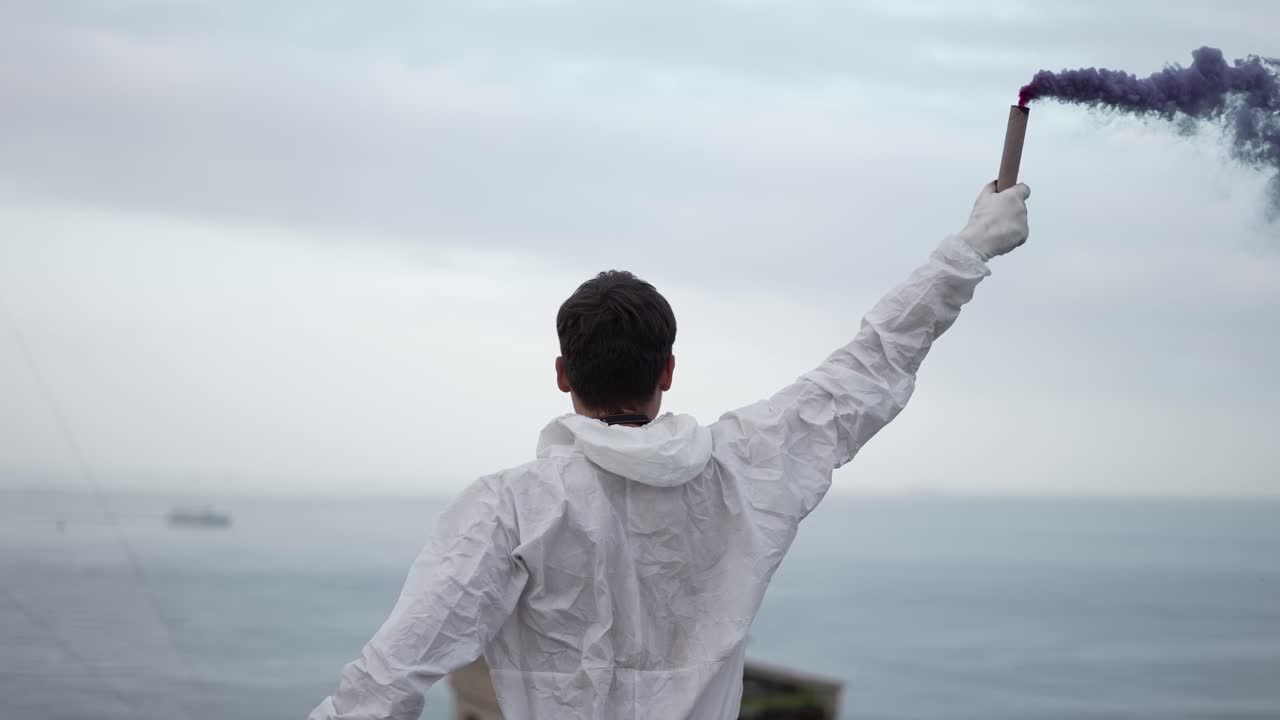 블루 스모크 스틱으로 지붕의 가장자리에 서 있는 보호복을 입은 남자