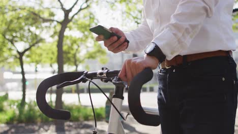 Mid-section-of-man-using-smartphone-while-holding-his-bicycle-on-the-street