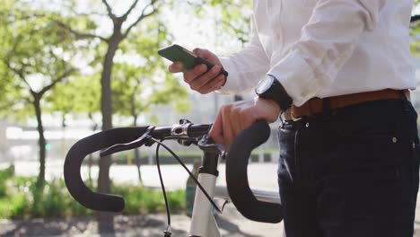 mid section of man using smartphone while holding his bicycle on the street