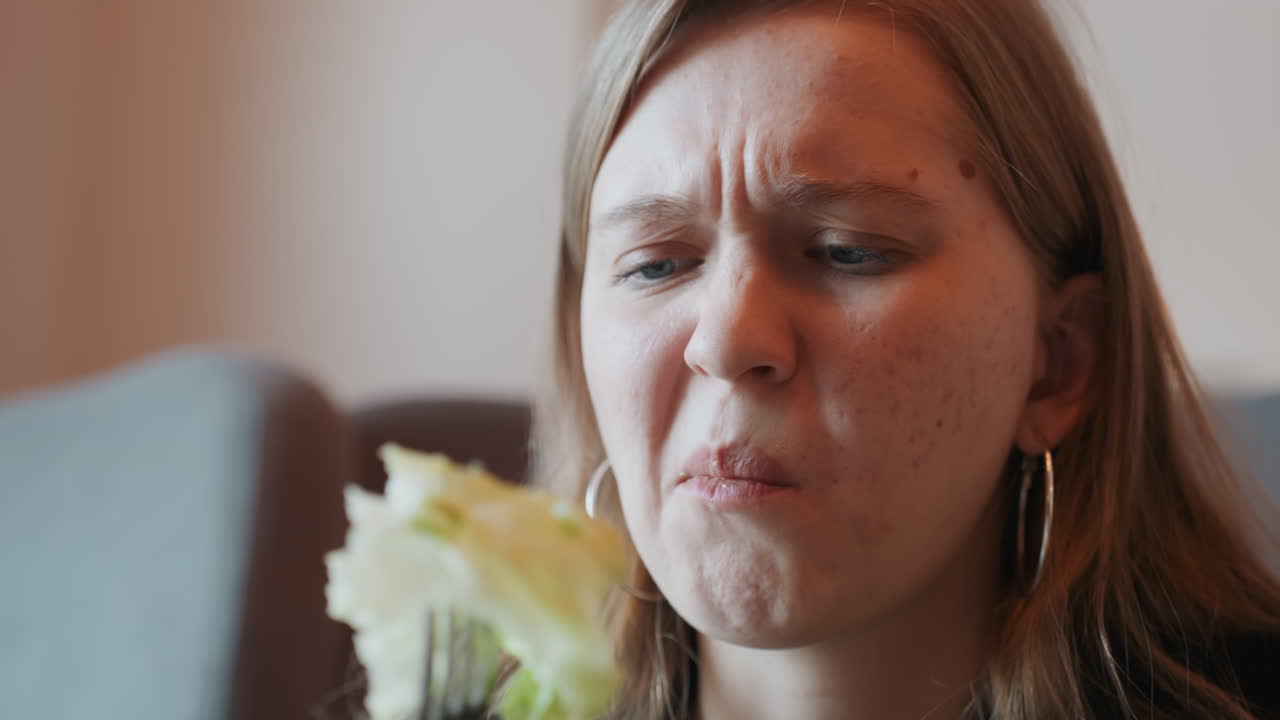 Mulher caucasiana fazendo careta após uma mordida, close-up de reação de mulher caucasiana mastigando salada com expressão amarga, garfo perto da boca, pele sardenta, mandíbula tensa, ambiente de sofá interno, sabor cru e espontâneo