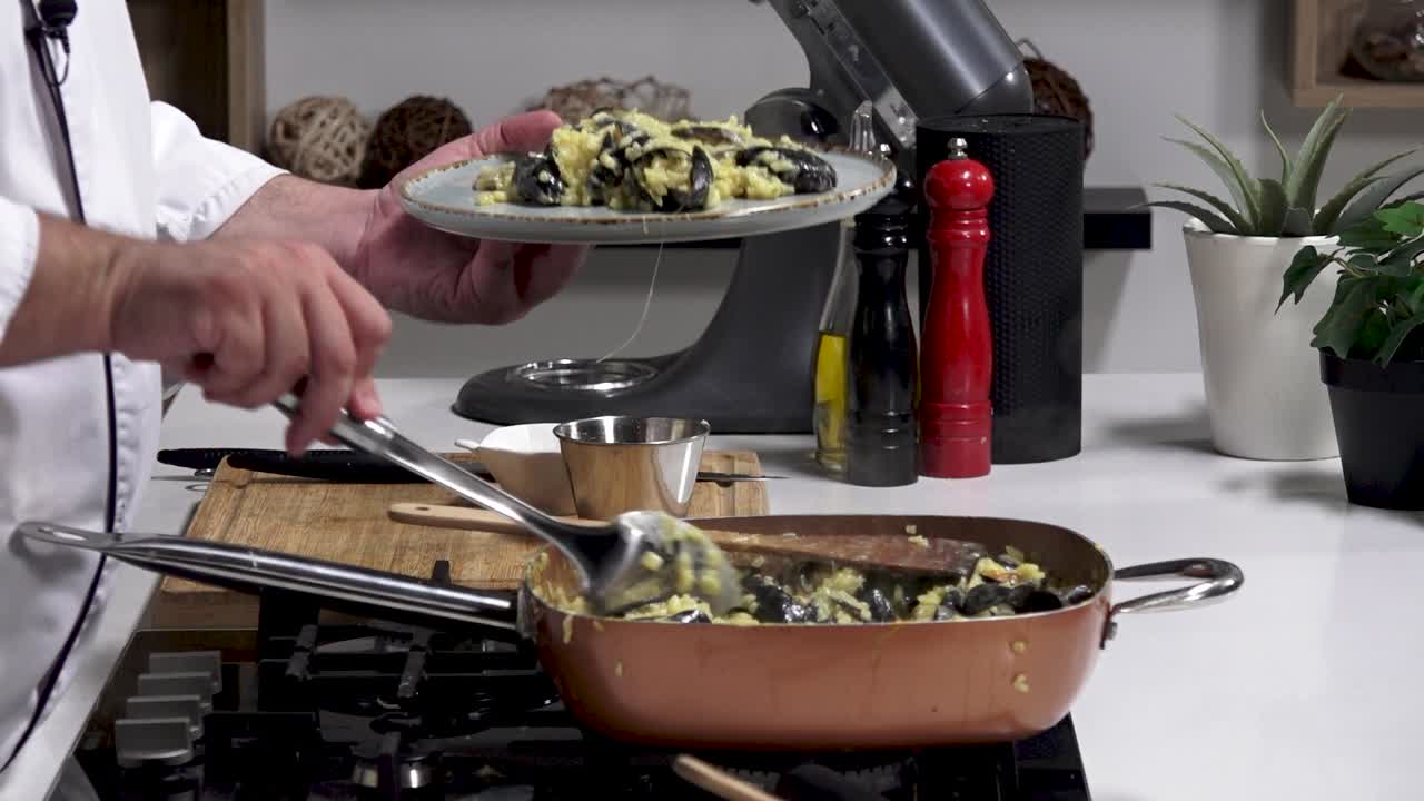 A chef prepares a delectable dish of black squid ink pasta mixed with fresh seafood and herbs. The preparation showcases cooking techniques and plating for a flavorful presentation