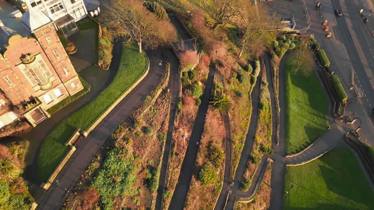 Aerial top down shot of thin curved paths in front of a castle during a sunny day in Scarborough, England