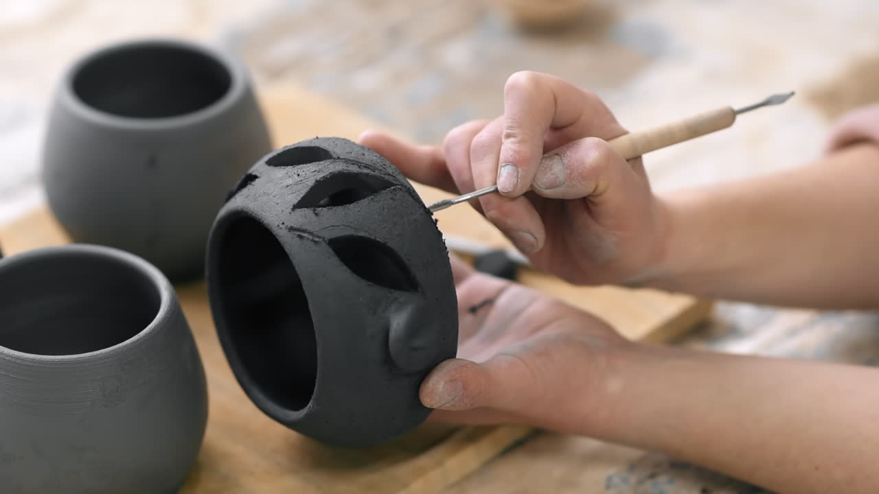 The master of sculpting pottery working in a studio. Cuts holes in fresh pottery. Slow motion