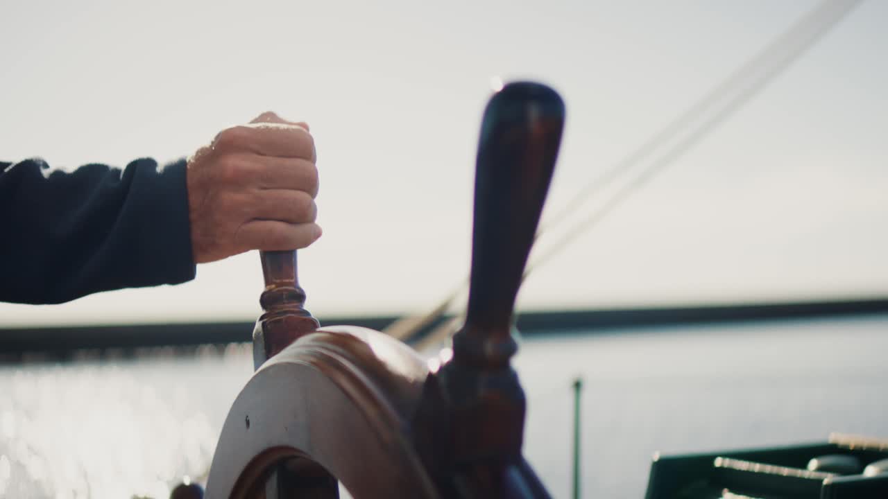 Hand steering wooden ship wheel on traditional sailing vessel under sunlight