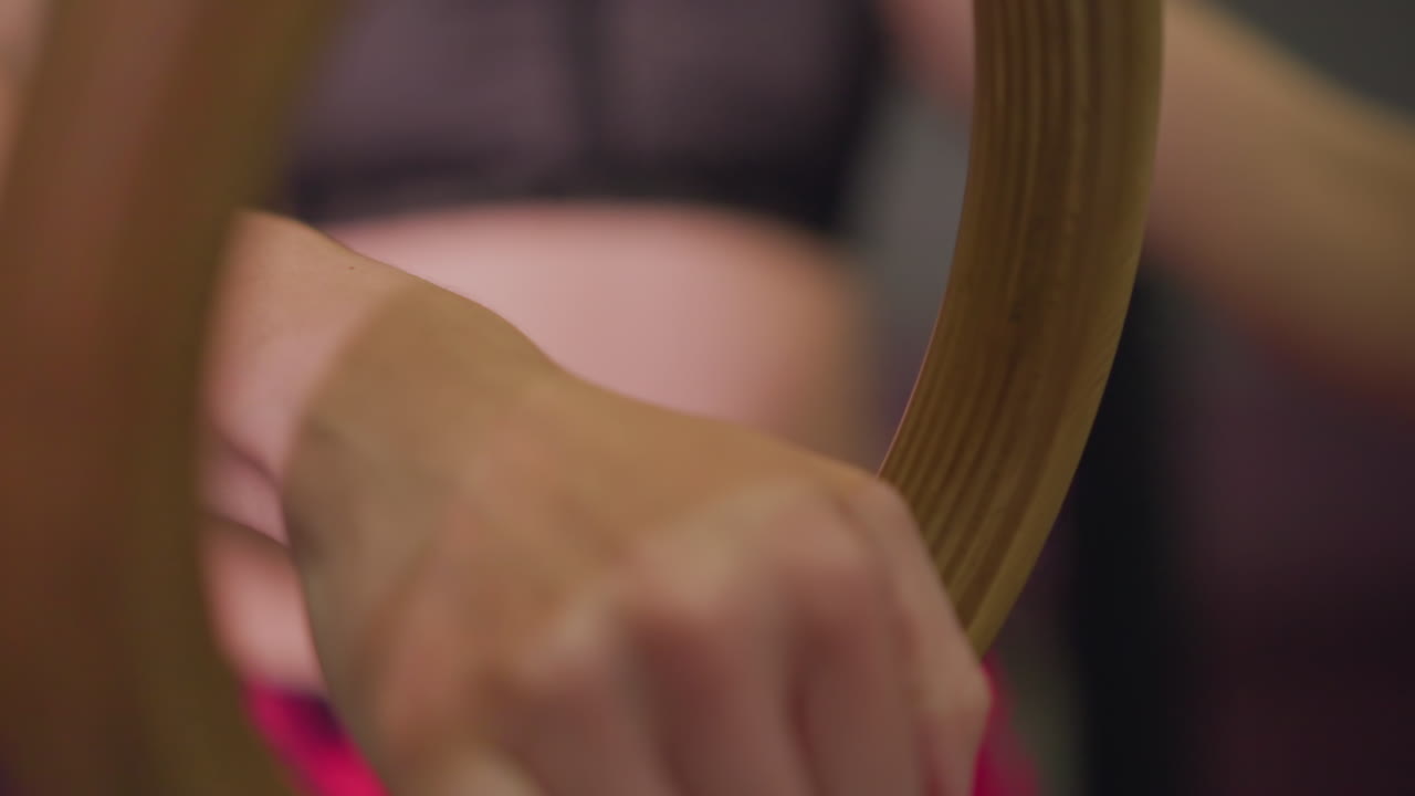 Donna inquadrata a mezzo busto che afferra anelli di legno, torso visibile e abbigliamento sportivo, allineamento controllato del polso in studio, riscaldamento ed esercizio di forza con ripetizioni concentrate e illuminazione soffusa da studio.
