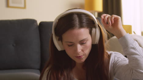 woman wearing wireless headphones sitting on floor at home streaming music from mobile phone 5