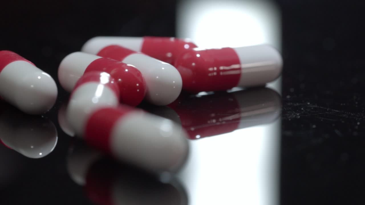 Pan left shot of red and white medicine capsules on reflective black surface, studio product detail