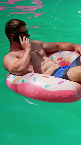 confident relaxed caucasian man speaks on the phone swimming in the pool. man sits in the inflatable circle having a conversation. vertical video