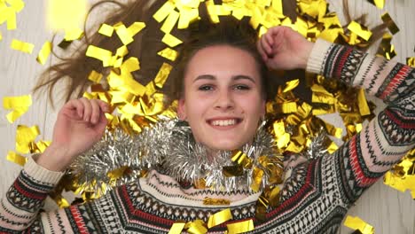 After-party-time:-Close-Up-view-of-young-happy-smiling-woman-lying-on-the-floor,-the-golden-confetti-falling-on-her.-Slow-motion