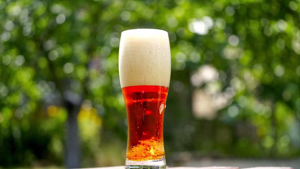 Glass of beer stands on a summer terrace. Full glass of dark beer with foam and small bubbles inside. Close-up.