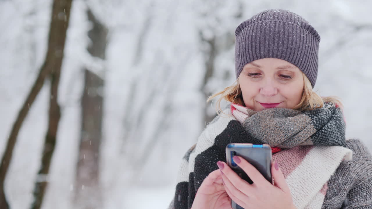 Giovane donna usa lo smartphone in un parco innevato.