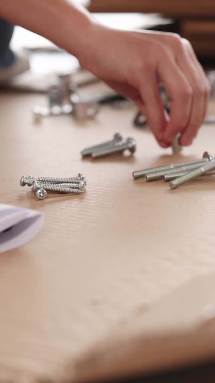 A vertical close-up showing hands sorting various metal hardware components on a light wooden surface