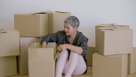 cheerful woman sitting on floor and unpacking cardboard boxes