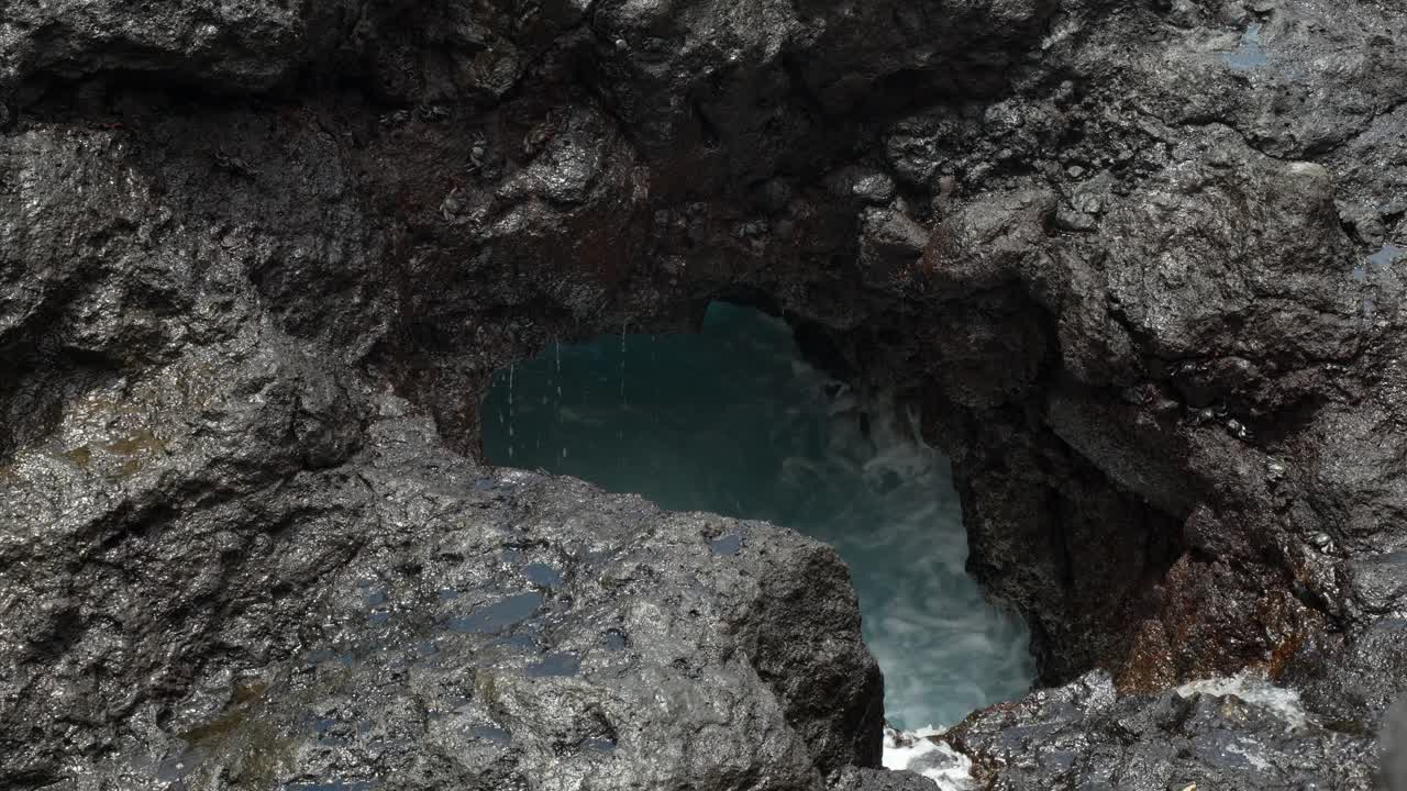 agujero de roca volcánica con olas de agua de mar salpicando en él, de cerca, tenerife