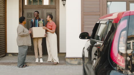 young man holding box walking with his mom and grandmother towards car before moving home