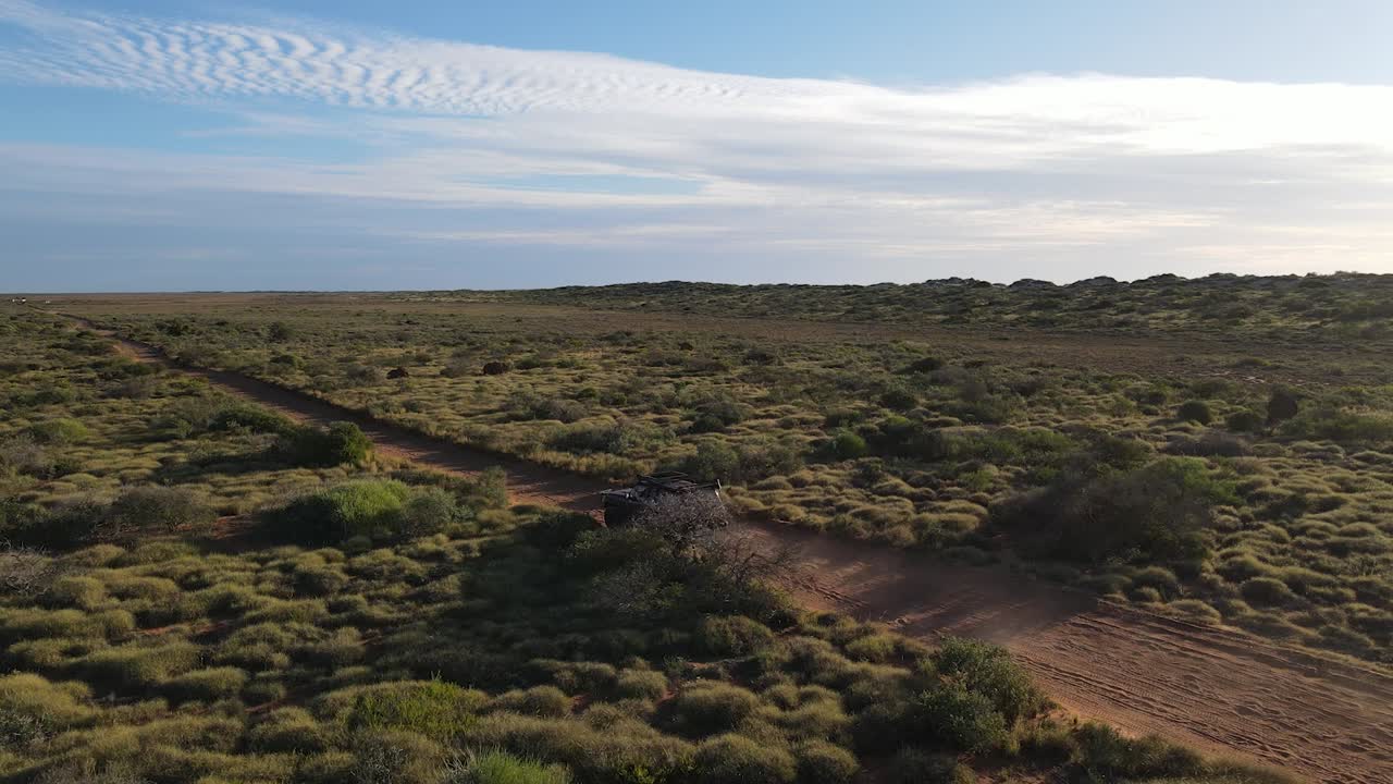 toma aérea de un vehículo de safari 4x4 conduciendo por una carretera rural en australia durante un día soleado con cielo azul