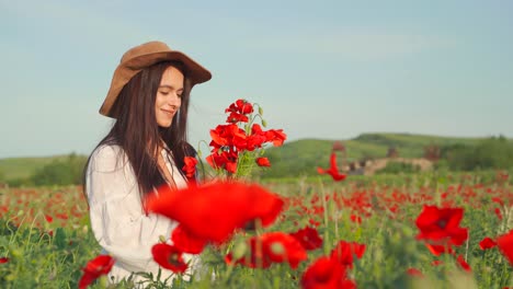 mujer caucásica con sombrero recoge ramo de amapola roja y huele flores en un campo pintoresco, de mano cerca