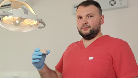 a dentist, with a beard, is holding a tooth in his hand in a dental office.