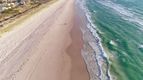 Two-people-walking-along-sandy-Tennyson-beach-in-Adelaide,-South-Australia-at-sunset