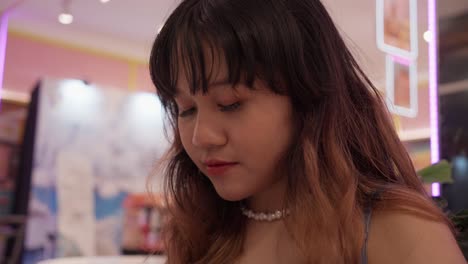 young indonesian girl dabbing on pink glossy lipstick.