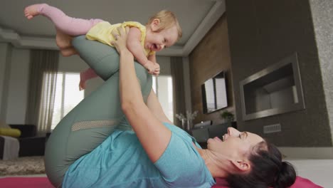 madre caucásica jugando con su bebé mientras practica yoga en la alfombra de yoga en casa