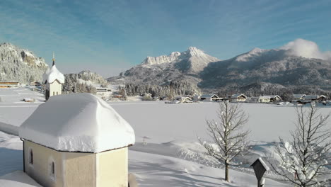 aerial drone shot showing a snowy landscape in in the sunshine of the tyrol, austria and revealing a snow covered tiny chapel in lechaschau