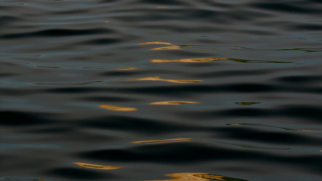 Una luce arancione si riflette sull'acqua scura, liscia e increspata.