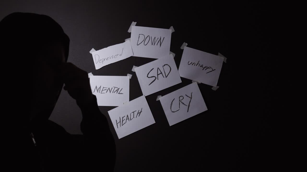 Sagoma di un uomo che si copre il viso con parole come "triste" e "depresso" sullo sfondo, a simboleggiare la lotta emotiva e i problemi di salute mentale.