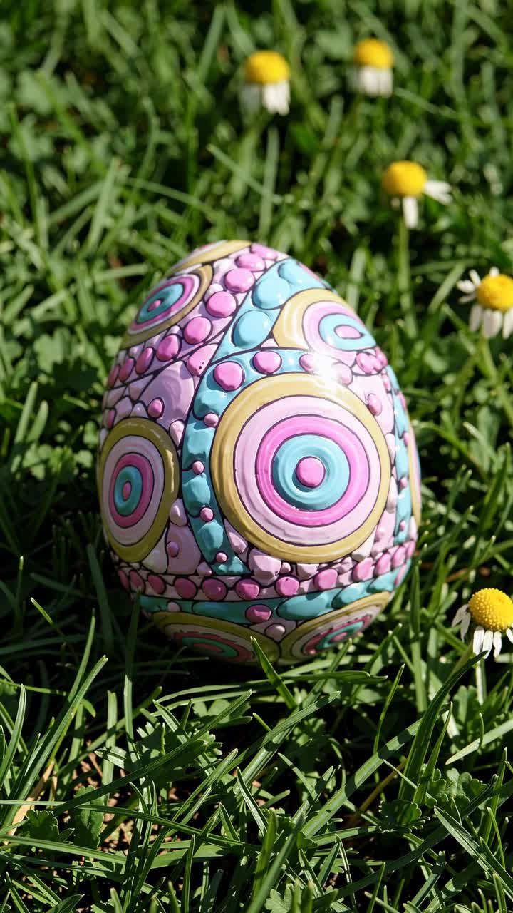 Videoaufnahme aus der Nähe eines bunten, aufwendig gemusterten Eis auf Gras, umgeben von kleinen Blumen