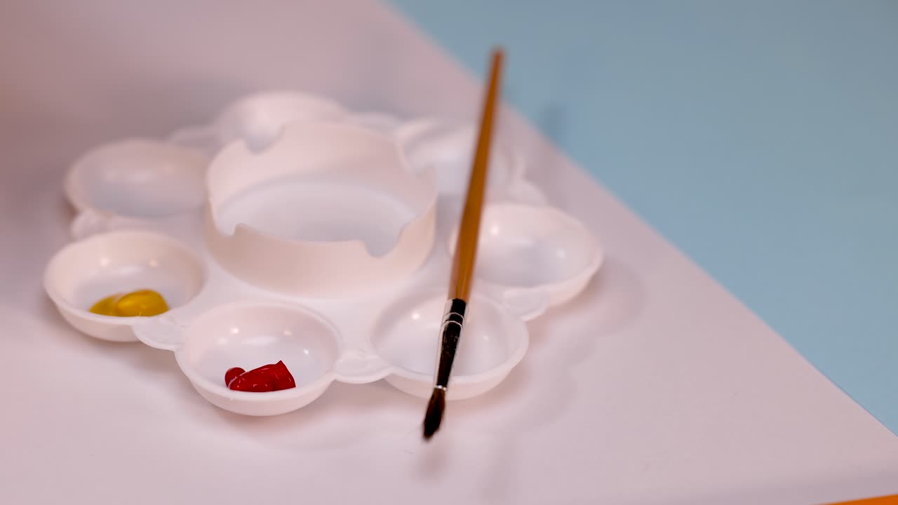 Hand dispenses yellow paint from tube into plastic palette, soft lighting, overhead static camera