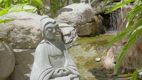 estatua budista en posición de loto en un hermoso jardín con un arroyo que fluye en el fondo