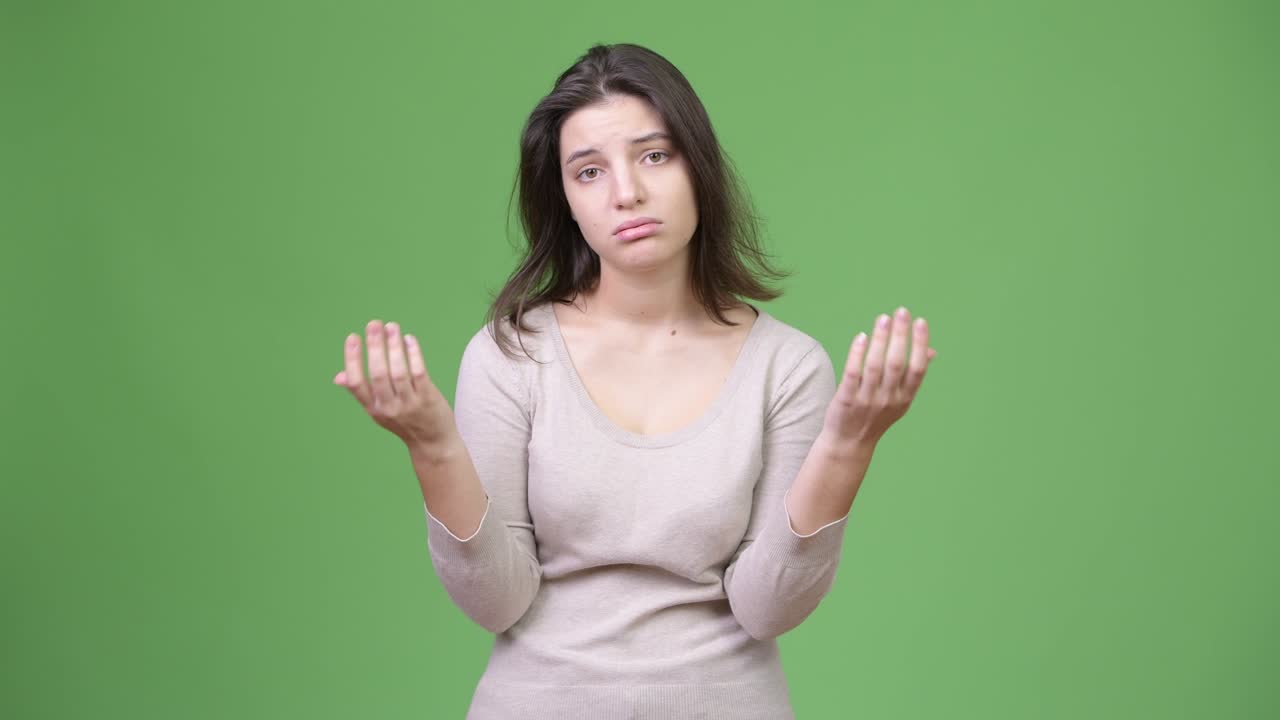 Young stressed woman shrugging shoulders against green background