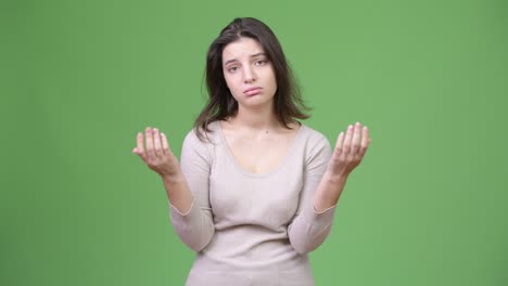 young stressed woman shrugging shoulders against green background