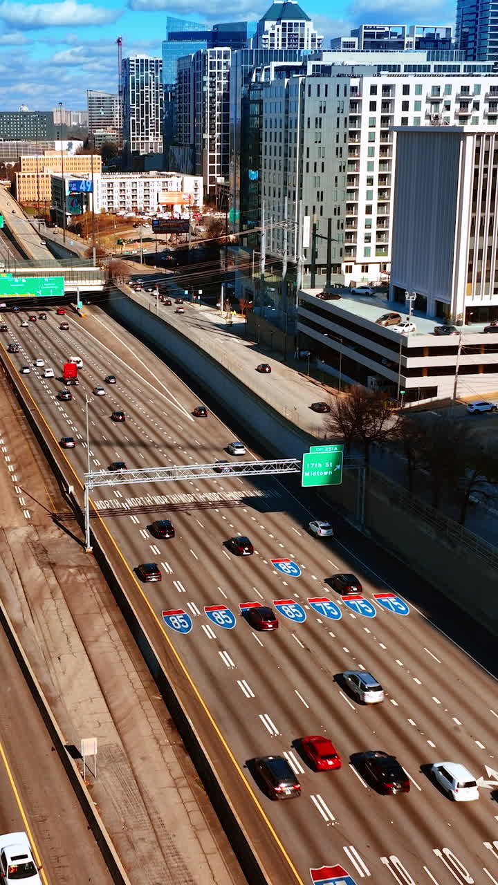 Multiple vehicles going by the busy wide-lane highways in Atlanta downtown. View on the city scenery on sunny day from top. Vertical video